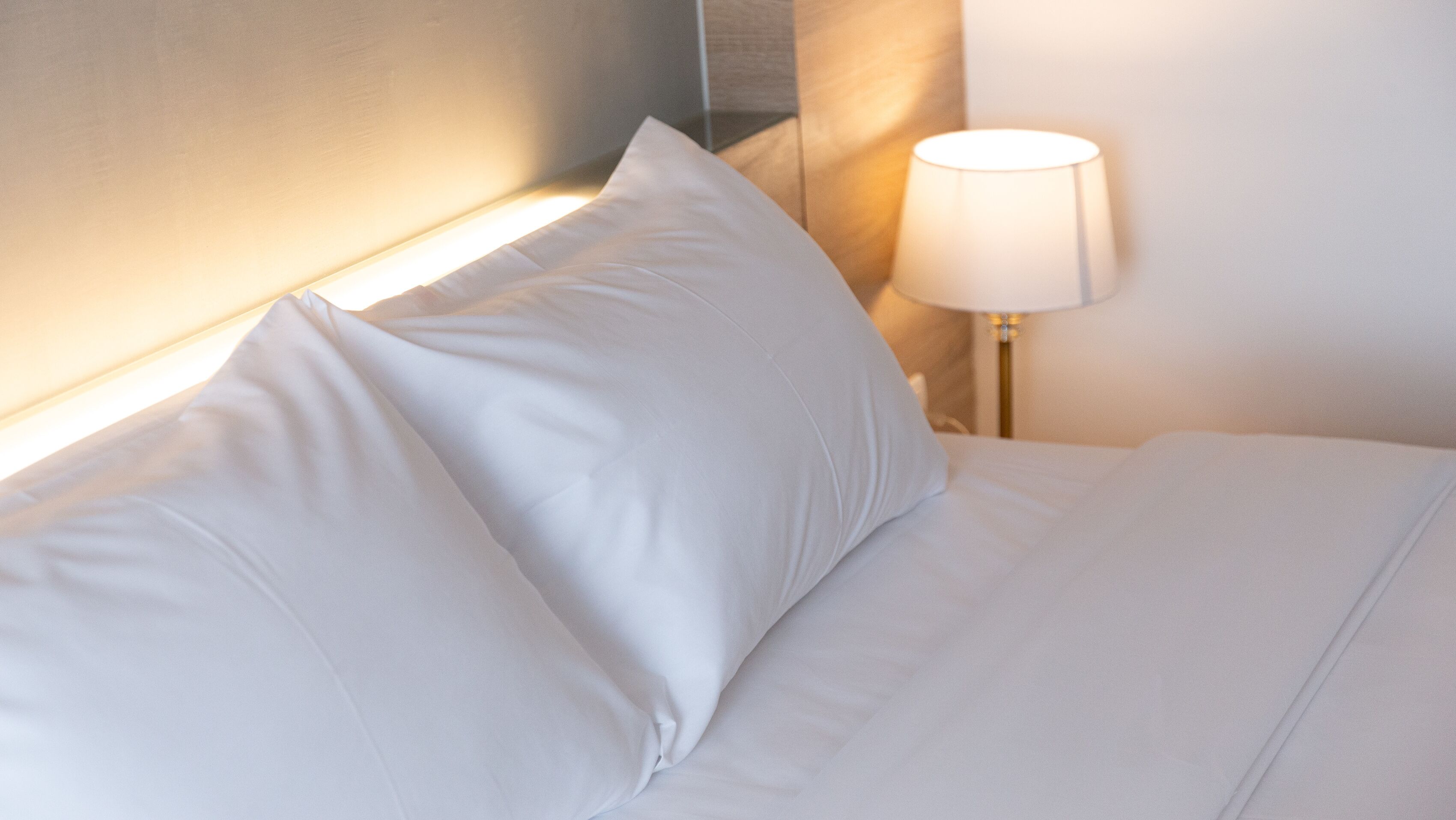 Un lit bien fait, avec du linge de lit blanc et des oreillers, une lampe de chevet et une tête de lit.