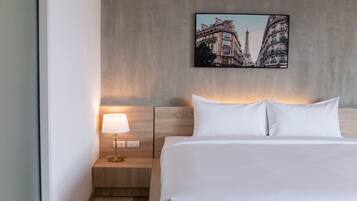 Habitación de hotel con una cama, una mesita de noche con lámpara y una fotografía de la Torre Eiffel en la pared.