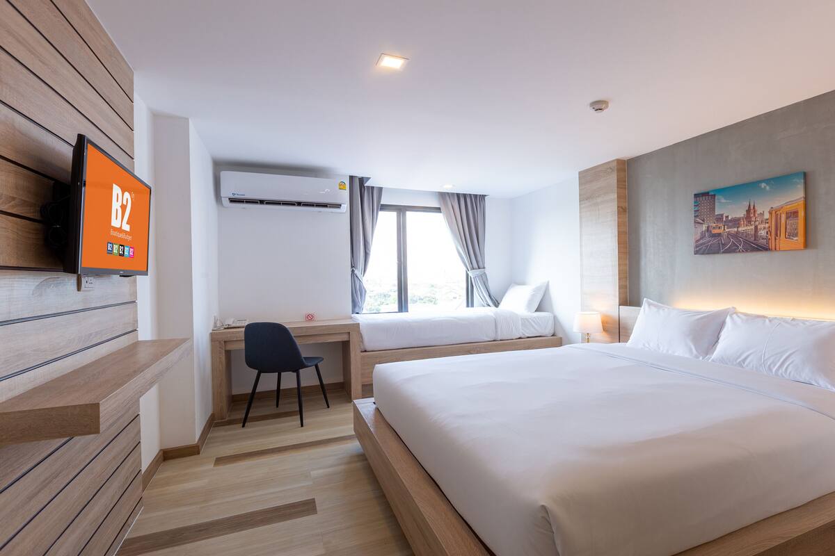 A hotel room with two beds, a desk, a TV, and a painting on the wall.