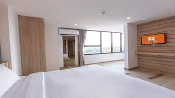 A modern hotel room with a large bed, a TV mounted on the wall, and a view of the city through large windows.