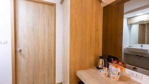A hotel room with a wooden door, a small table with a kettle, cups, and bottles, and a mirror above a sink. - B2 Rayong Boutique and Budget Hotel (Rayong)