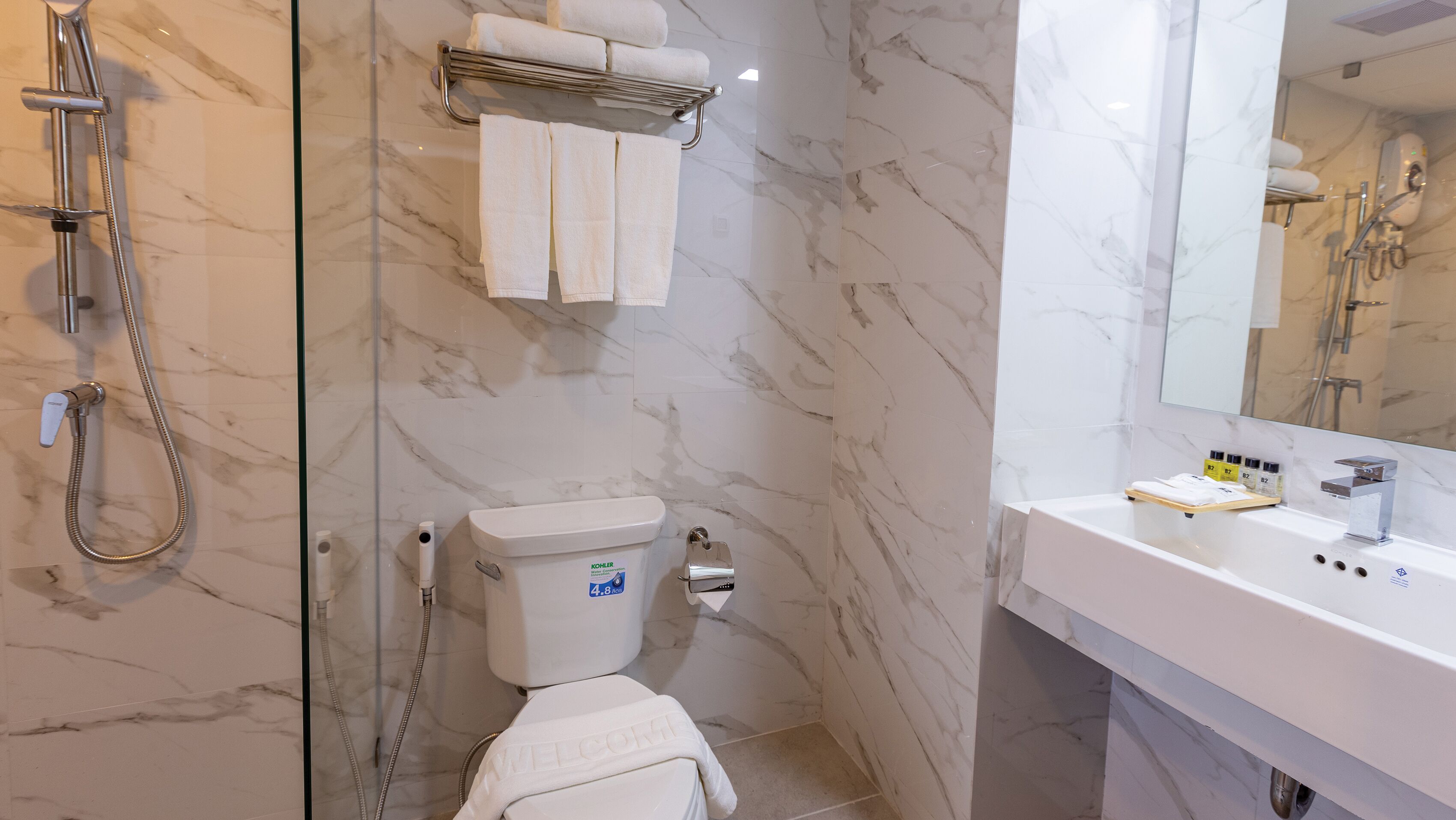 A bathroom with a marble floor, a toilet, a shower with a handheld showerhead, a sink with a mirror, and a towel rack with towels.