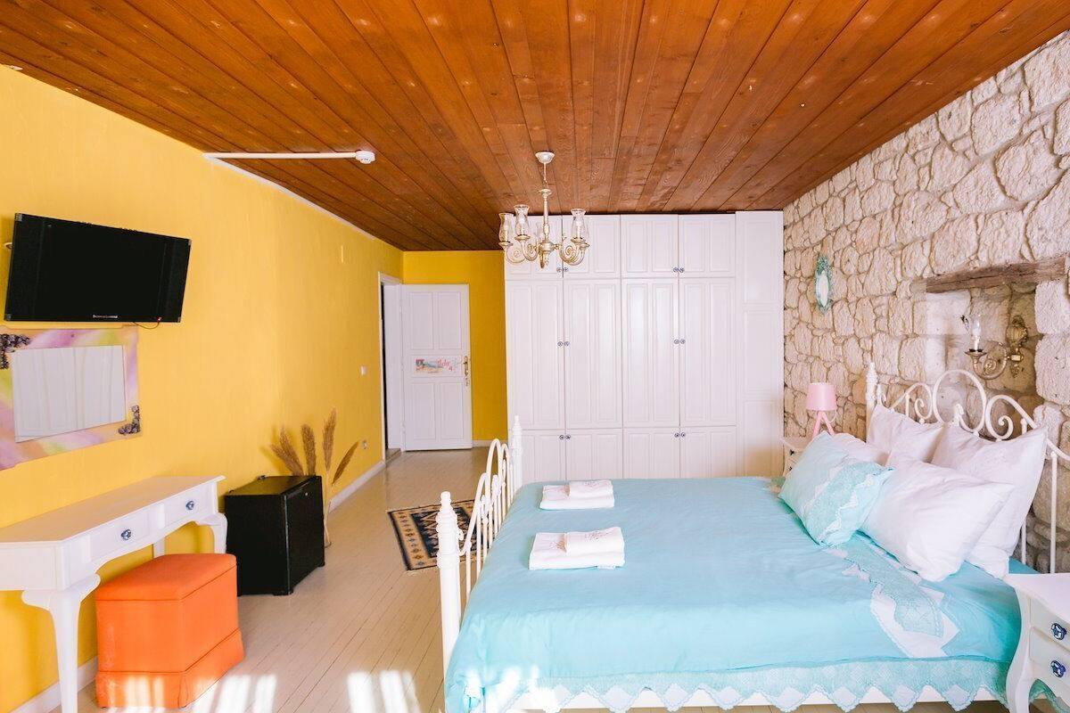 Un dormitorio con pared de piedra, una cama con ropa de cama azul, un armario blanco y un televisor en la pared.