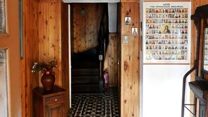 Een houten interieur met betegelde vloer, een trap en een muur met een poster van religieuze figuren.