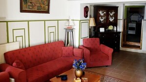 Een woonkamer met een rode bank, een bijzettafeltje met een vaas, een schilderij aan de muur, en een houten kast met een klok.