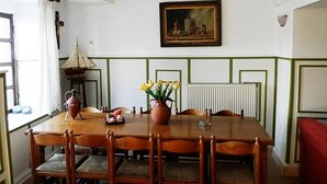 Een eetkamer met een houten tafel, stoelen, een vaas met bloemen, een schilderij aan de muur en een radiator.