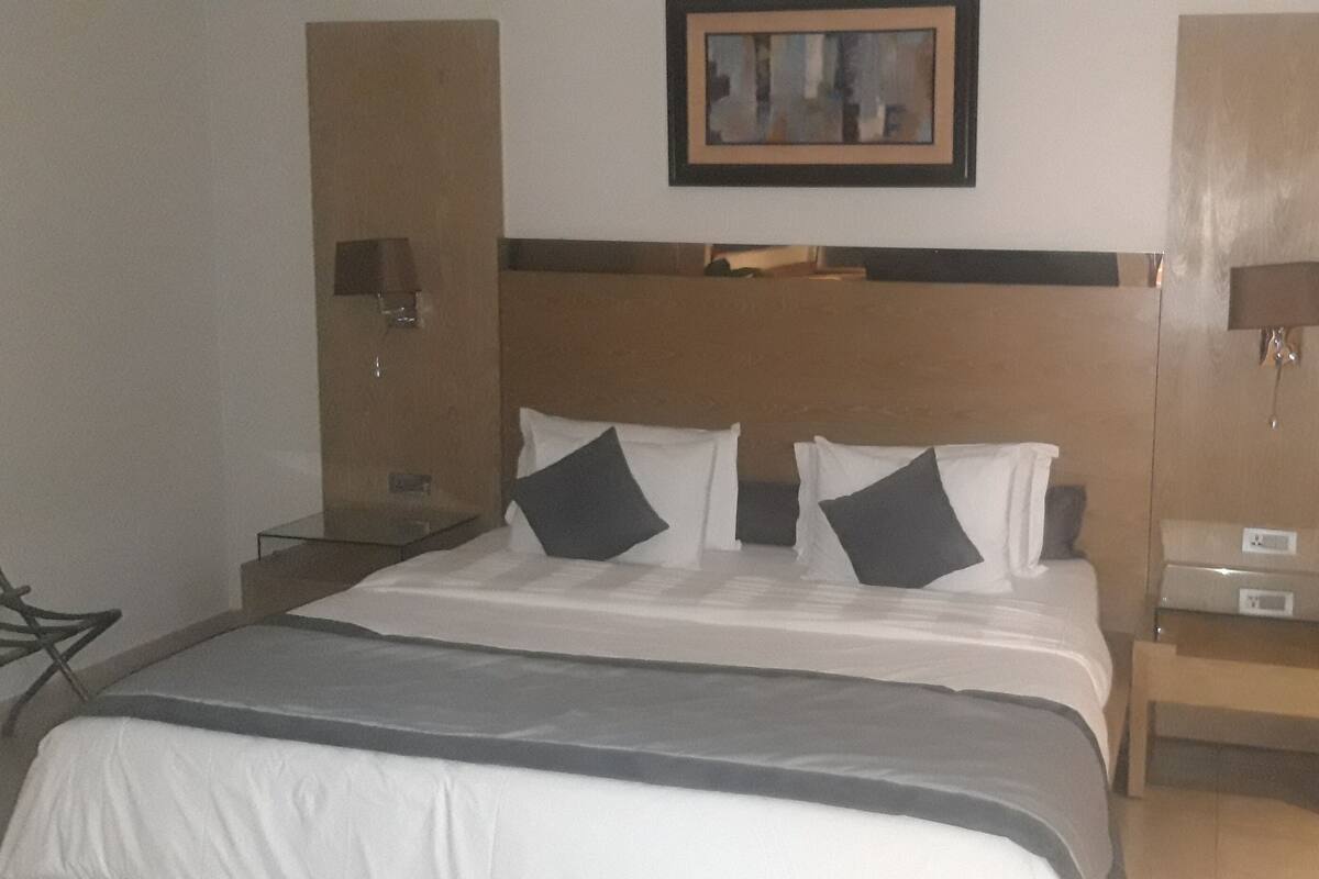 Una habitación de hotel con una cama grande, dos mesitas de noche, una lámpara de noche, una silla y un cuadro en la pared.