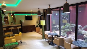 Un hall d’hôtel comprenant des espaces de détente, un comptoir d’accueil, un téléviseur et une grande fenêtre agrémentée de plantes.