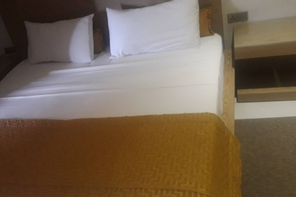 Una cama con ropa de cama blanca y una manta marrón.