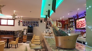 Un espace bar agrémenté d’une grande bouteille de champagne Moët & Chandon, de tabourets de bar et d’un écran de télévision diffusant des images de plats.