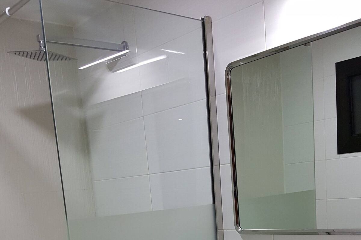 Un baño con cabina de ducha de vidrio, un lavabo blanco y un espejo encima.