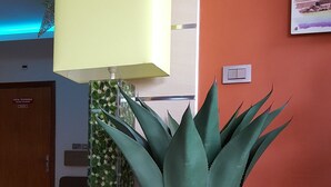 A reception area with a wooden planter box containing a large green plant, a modern lamp, and a small Christmas tree. - Hotel VDN by Good Rade (Dakar)