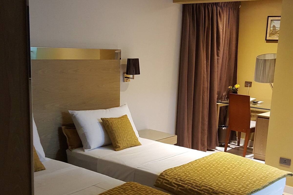 Una habitación de hotel con dos camas, un escritorio, una silla y una lámpara.