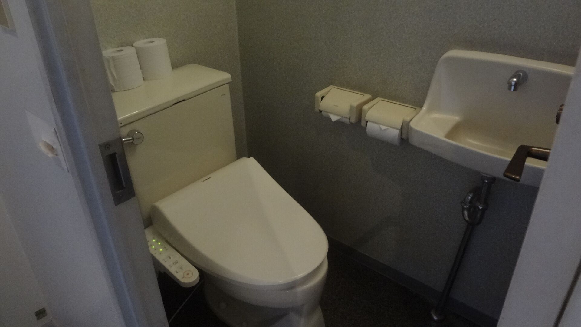 Casa de banho pequena e compacta, com sanita, bidé e rolo de papel higiénico na parede.