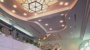 A modern interior with a central escalator, a unique geometric ceiling light fixture, and a curved wall design. - Hamanako Kanzanjionsen Hotel Kikusuitei (Hamamatsu)