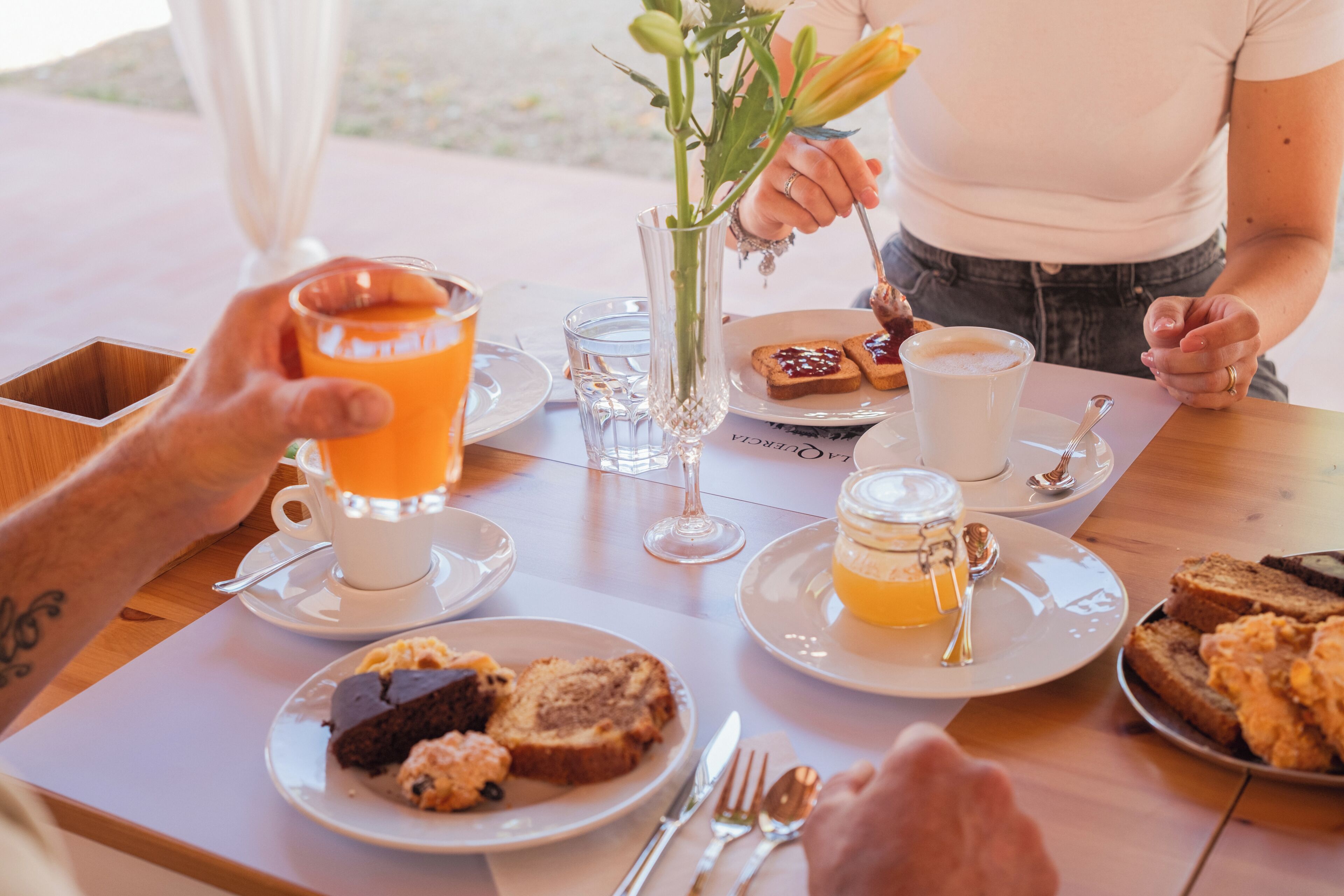 A dining table with plates of food, a glass of orange juice, a vase with flowers, and a cup of coffee.