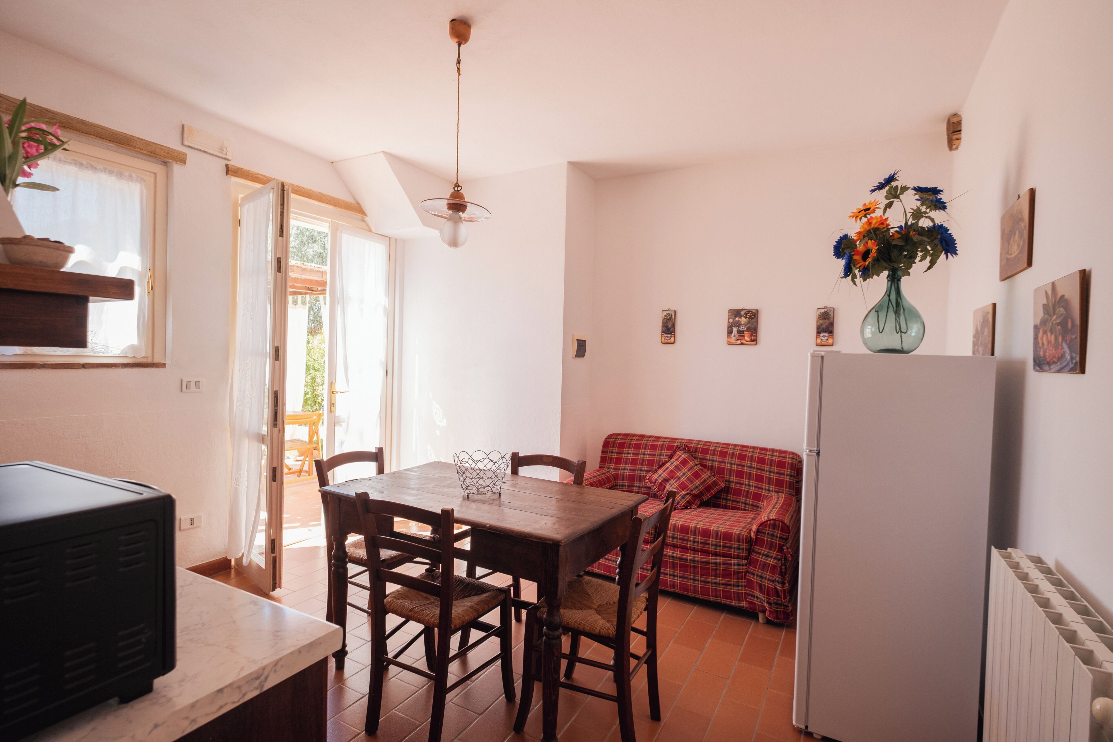 Una cocina compacta con una mesa de comedor, sillas, un refrigerador y un sofá rojo a cuadros.