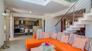 A modern living room with an orange sofa, a coffee table with a floral vase, and a staircase with a red railing. - Villa retreat in the heart of Cretan nature (Rethimno)