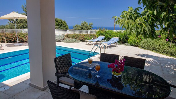 A poolside area with a glass table, wicker chairs, and lounge chairs. - Villa retreat in the heart of Cretan nature (Rethimno)