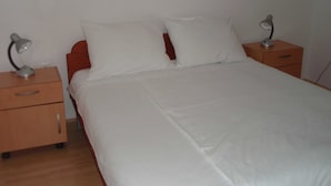 A neatly made bed with white linens, two bedside tables with lamps, and a wooden headboard. - Apartment Luna (Konavle)