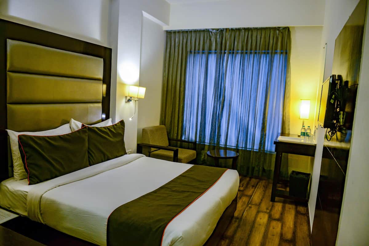 A hotel room with a large bed, a desk, a chair, and a window with curtains.