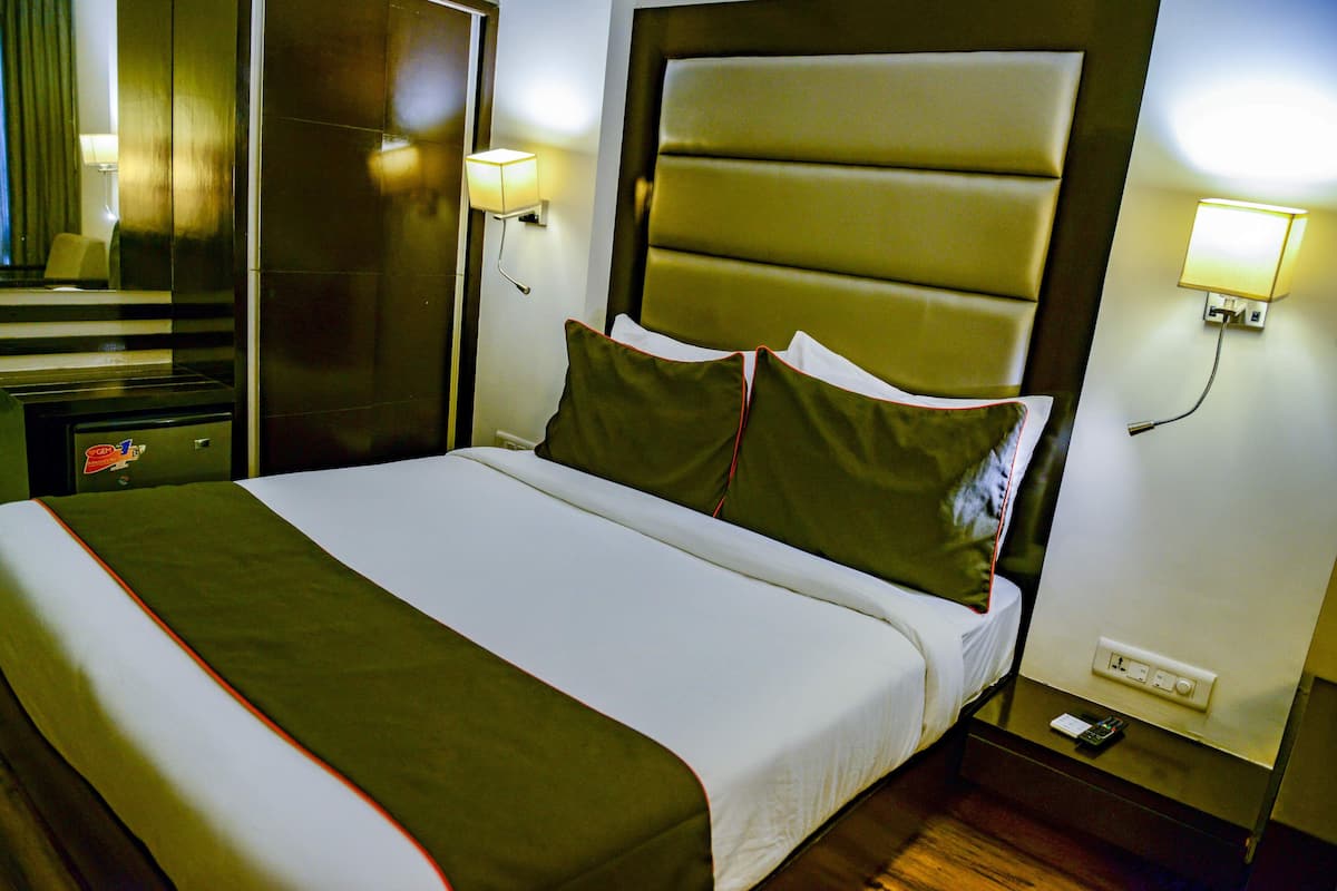 A hotel room with a large bed, a nightstand, a lamp, and a wall-mounted light.