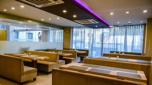Um restaurante com cabines e mesas, janelas amplas com cortinas leves e um design moderno no teto.