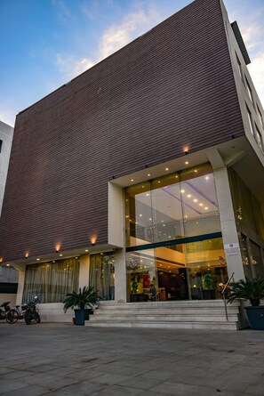 A modern building with a large glass entrance, steps leading up to the door, and potted plants in front. - Hotel Veronica (Vadodara)