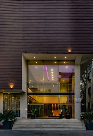 Un edificio moderno con entrada de vidrio, escalones que lo conducen y plantas en macetas en la base.