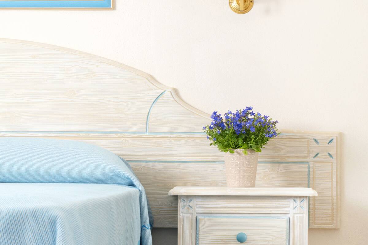 Ein Schlafzimmer mit einem Bett mit blauer Bettwäsche, einem Nachttisch mit einem Blumentopf und einer Wandleuchte.