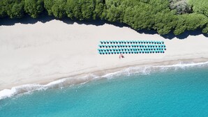 Vista aérea de una playa con una hilera de sombrillas azules y blancas y una persona con una camisa roja.
