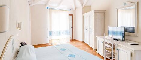 Une chambre à coucher avec un lit, un téléviseur posé sur un meuble et une fenêtre avec des rideaux.