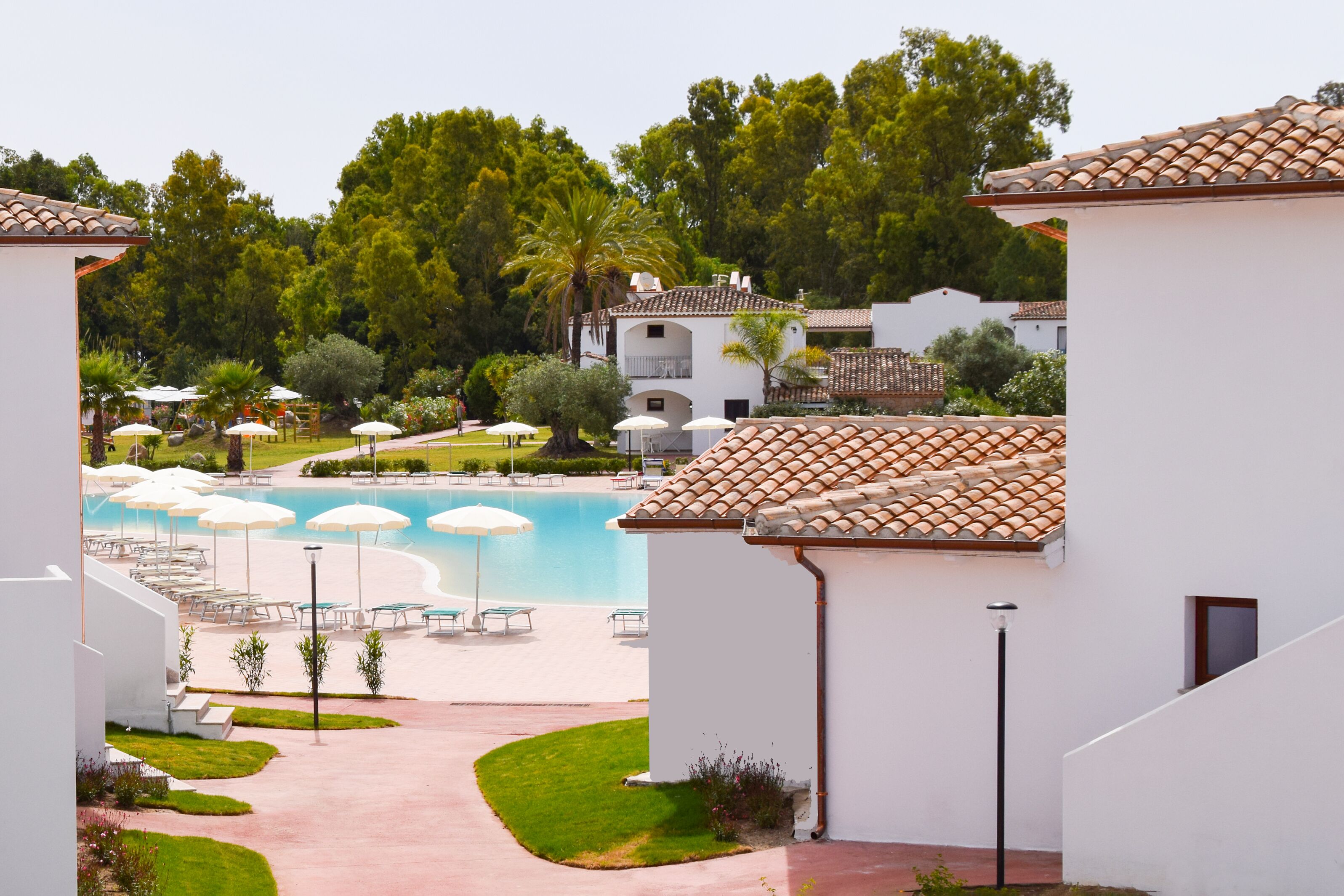 Un complejo turístico con piscina, tumbonas y edificios blancos con tejados de cerámica.