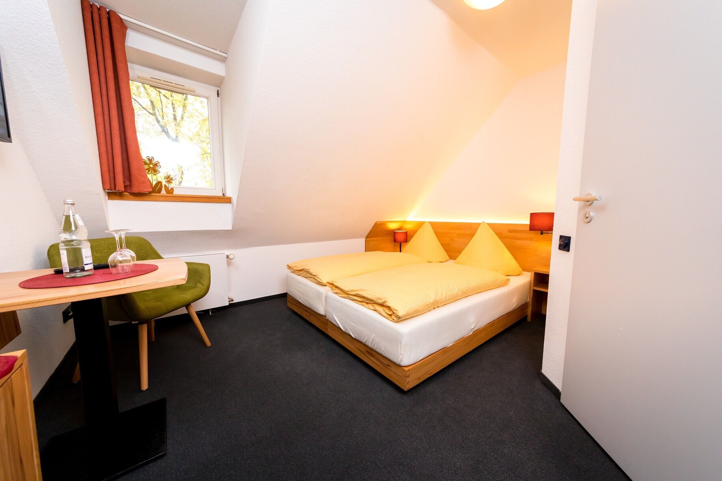 A compact hotel room with a single bed, a small desk, and a chair.