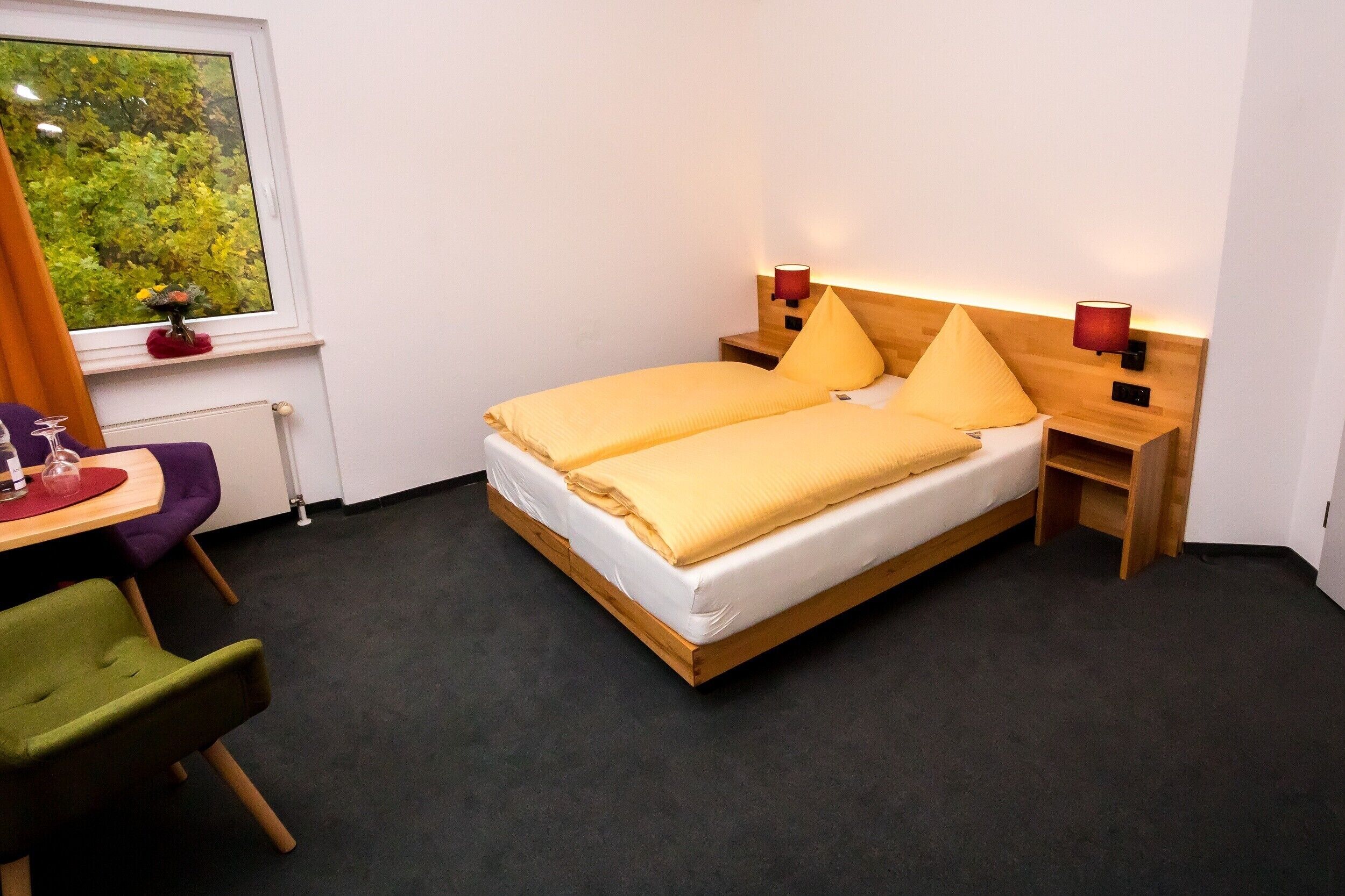 Een slaapkamer met een bed, nachtkastjes, een stoel, een raam met uitzicht en een tafeltje met een vaas.