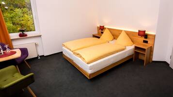 Een slaapkamer met een bed, nachtkastjes, een stoel, een raam met uitzicht en een tafeltje met een vaas.