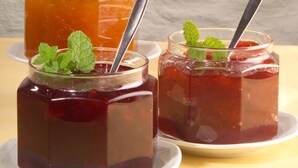 Three glass jars of jam with metal spoons and mint leaves on a table.