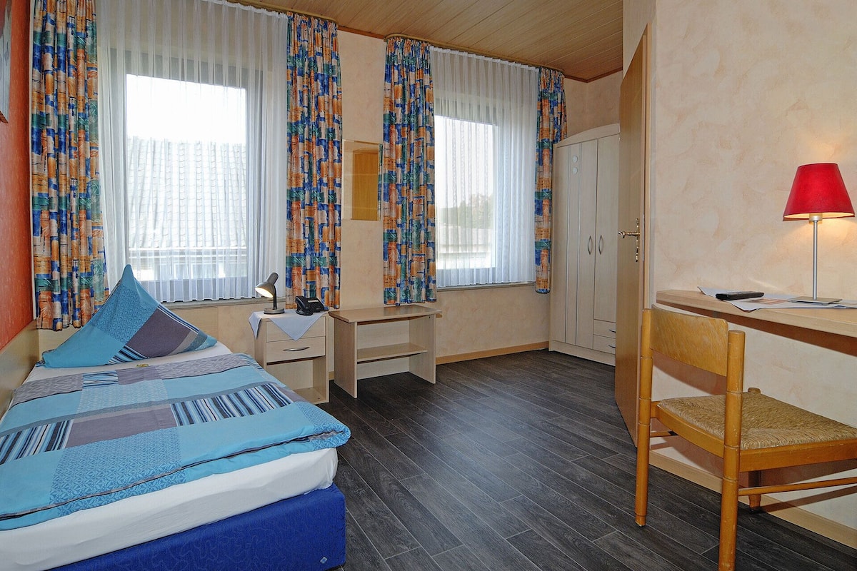 Una habitación de hotel con cama, escritorio, silla y lámpara.