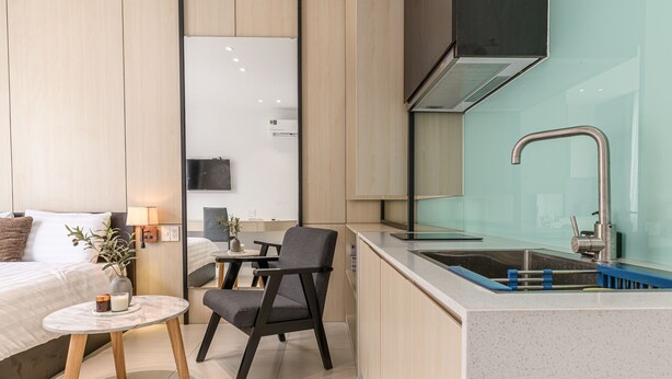 A compact kitchen with a modern design, featuring a built-in sink, a dining area with a small table and chair, and a visible television in the background. - Sumi Home (Da Nang)