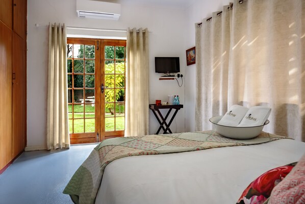 Un dormitorio con cama, televisor, una mesita con un frutero de toallas y una puerta que da a un jardín.