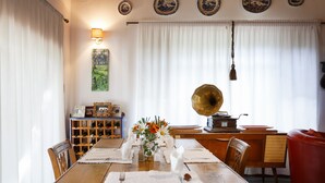 Een eetruimte met een houten tafel gedekt voor vier personen, omringd door stoelen. Een vintage gramofoon en een wandlamp zijn zichtbaar.