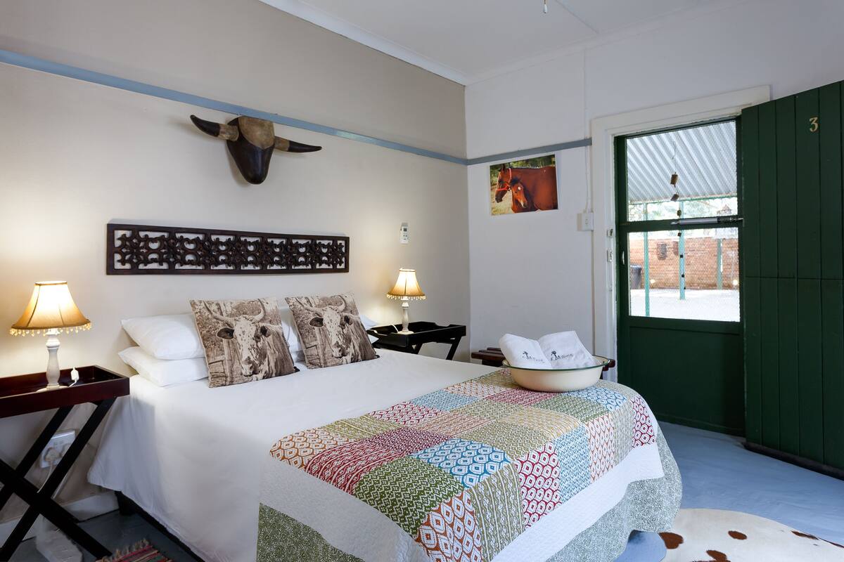 A hotel room with a bed, two bedside tables, a lamp, a decorative wall piece, a door, and a window.