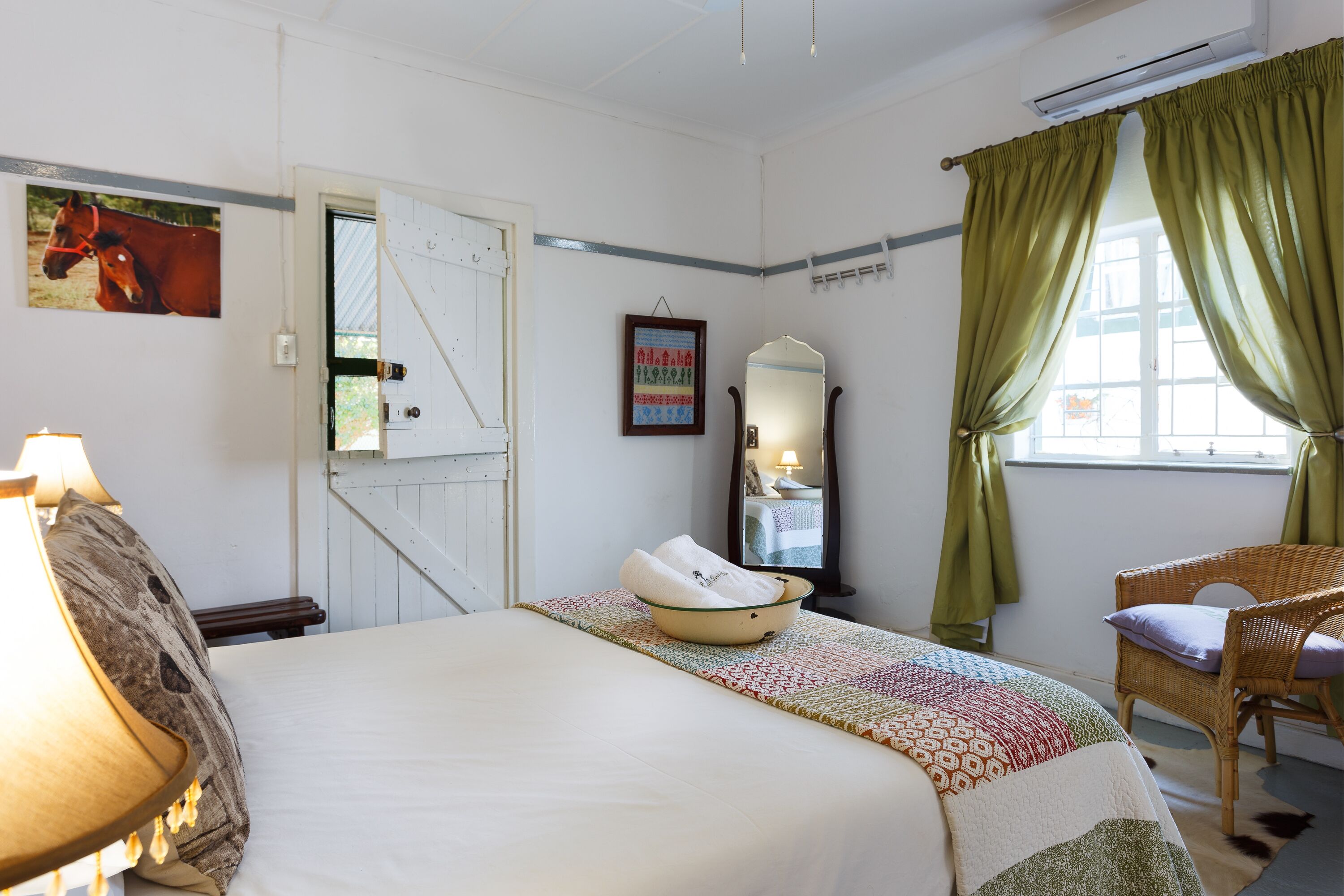 A bedroom with a bed, a chair, a mirror, a window with curtains, and a wall with a picture.