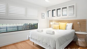 Une chambre à coucher moderne avec un grand lit, du linge de lit blanc et une vue sur un jardin clos, visible par la fenêtre.