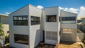 Une maison moderne à deux étages, dotée de grandes fenêtres, d’une terrasse en bois et d’un jardin clôturé.