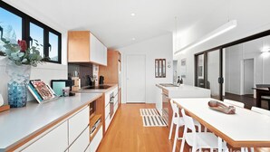 Une cuisine moderne avec des meubles blancs, un plan de travail en bois et un coin repas comprenant une table et des chaises blanches.