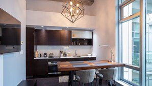 A modern kitchen with dark wood cabinets, a central island with bar stools, and a large window providing natural light. - Hudson Hideaway-Historic Hudson Building in Beautiful Downtown Victoria by Victoria Prime! (Victoria)