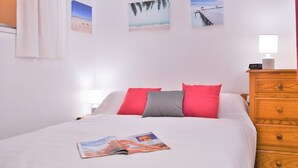 Ein Schlafzimmer mit einem Bett, einer hölzernen Kommode und drei an der Wand befestigten Bildern, die Strandansichten zeigen.