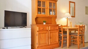 Ein gemütlicher Wohnraum mit Holzschrank, Fernseher, Esstisch mit Stühlen und Spiegel.