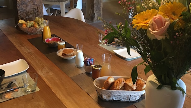 Een houten eettafel met diverse gerechten en drankjes, een vaas met bloemen, en een rustiek interieur met stenen muren en houten balken.